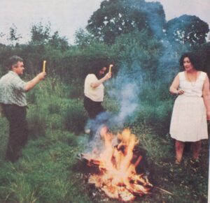 Eleanor Bone, a woman, and Bill Bone dancing around a fire in a field, while holding a candle.